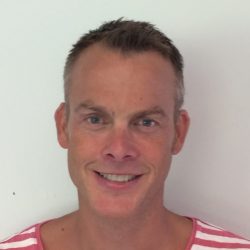 Mann med et vennlig smil iført en stripet rosa og hvit skjorte mot en vanlig hvit bakgrunn. Foto Mikael Flygind Larsen.