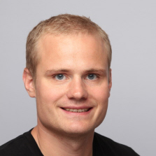 Et profesjonelt hodebilde av Mikael Flygind Larsen smilende med kort hår mot en nøytral bakgrunn.