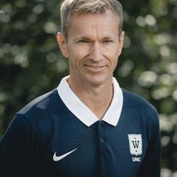 En selvsikker mann i sportspoloskjorte poserer med et lite smil mot et bakteppe av grønt løvverk, fotografert av Grete Etholm.