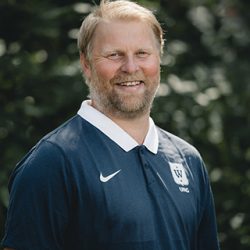 En smilende Fredrik Aukland med lyst skjegg, iført mørk poloskjorte med logo på, stående utendørs med frodig grønt i bakgrunnen.