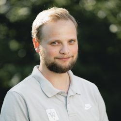 En mann med et vennlig smil, med kort skjegg, i en uformell poloskjorte, satt mot en uskarp naturlig bakgrunn, utstråler en avslappet og positiv stemning som Marius Marcussen.