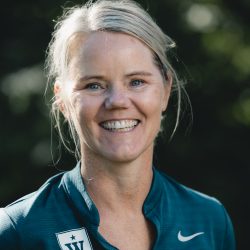 En smilende kvinne utendørs iført en sportsjakke med Nike-logo og et merke som ser ut til å ha en "W" på seg, noe som muligens indikerer tilknytning til Mette Lia-laget eller skolen.
