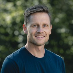 En smilende Kristian Horntvedt med kort hår utendørs, som utstråler selvtillit og vennlighet.