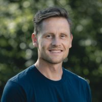 En smilende Kristian Horntvedt med kort hår utendørs, som utstråler selvtillit og vennlighet.