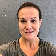 En kvinne med håret trukket tilbake, iført en grå topp, smilende lett for en uformell selfie med en nøytral farget vegg i bakgrunnen. Dette er Marita Hjelmungen.