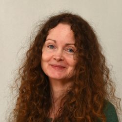 En kvinne med langt krøllete hår og et mildt smil, iført en grønn topp, mot en nøytral bakgrunn.