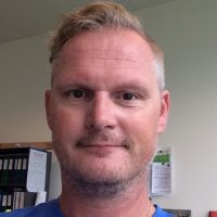 Erik Hæren, en mann med kort skjegg og bart med et vennlig, subtilt smil, med kort, pent kjemmet hår. Han ser ut til å være i et kontormiljø, gitt