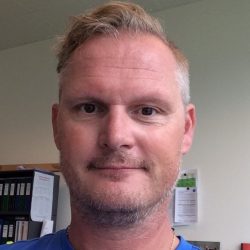 Erik Hæren, en mann med kort skjegg og bart med et vennlig, subtilt smil, med kort, pent kjemmet hår. Han ser ut til å være i et kontormiljø, gitt
