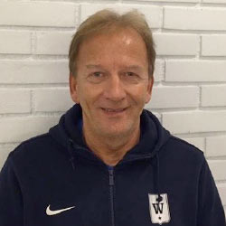 En smilende person ved navn Erik Andersen, iført en mørkeblå Nike-sportsjakke med et "w"-emblem, poserer foran en hvit murvegg.