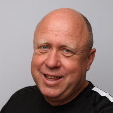 En munter, skallet mann ved navn Knut Norgren med et vennlig smil, iført svart skjorte mot grå bakgrunn.