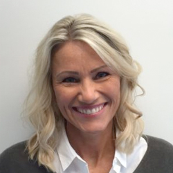 En blid kvinne ved navn Kristin Kristoffersen med et lyst smil, blondt mellomlangt hår, iført profesjonell hvit skjorte og grå genser.