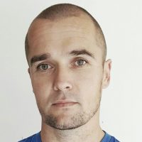 Et nærbilde av Lars Olsen, en mann med kort hår og et nøytralt uttrykk, iført blå skjorte, mot hvit bakgrunn.