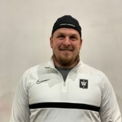 En smilende Lasse Arnesen iført svart lue og hvit sportsjakke med logo.