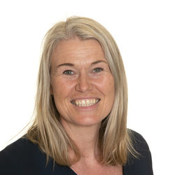En smilende kvinne med langt blondt hår, iført en mørk topp, mot hvit bakgrunn er Linda M Næsheim.