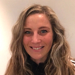 Et portrett av Mona Christine Holm, en smilende kvinne med bølget, blondt hår og slående blå øyne.