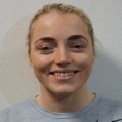 En smilende kvinne, Sara Martinsen, med håret bakbundet, iført en tilfeldig grå topp, som utstråler positivitet.