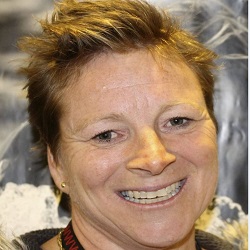 En person med kort hår og et gledesfullt smil står mot et svakt mønstret bakteppe, og utstråler varmen og ynden knyttet til navnet Unn Merete L. Jæger.