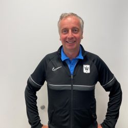 En smilende mann iført Niklas Diethelm-sportsjakke med logo på brystet, poserer mot en hvit veggbakgrunn.