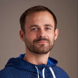 Portrett av Eirik Andreas Mork, en smilende mann med skjegg, iført blå hettegenser mot nøytral bakgrunn.