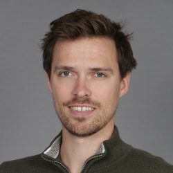 Et portrett av Emil Marøy med et selvsikkert smil, med kort brunt hår og en lys skjeggstubber, iført en uformell glidelåsgenser mot en nøytral grå bakgrunn.