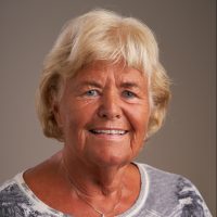 Et portrett av en smilende eldre kvinne med blondt hår som utstråler varme og glede på Gro Maastad.