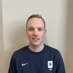 En ung mann, Lars Frederic Nordbakken, i en mørk Nike-genser med logo på venstre bryst, poserer for et bilde mot en vanlig lys vegg.