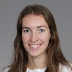 En smilende kvinne, Ingrid Sørum, med langt brunt hår og hvit topp, utstråler positivitet i et profesjonelt portrett.