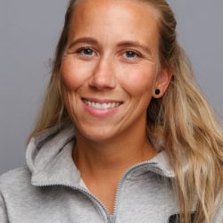 En smilende kvinne med langt blondt hår, iført en grå hettegenser og små ringøredobber, mot en nøytral bakgrunn.