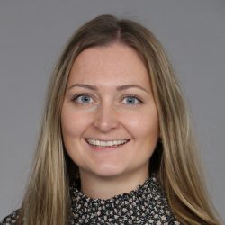 Et portrett av Maren Gulbrandsen, en smilende kvinne med langt blondt hår, iført en svart topp med spettet mønster. Hun ser ut til å ha en vennlig væremåte, og bakgrunnen er det