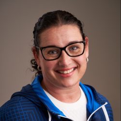 En kvinne, antatt å være Maria C.B. Mathisen, med briller og blå jakke smiler til kameraet.