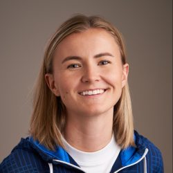 En smilende kvinne, Pernille Krathe, med kort blondt hår, iført en blå hettegenser med hvit og blå kant.