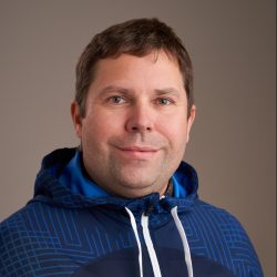 Portrett av Sindre Lien smilende, iført en blåmønstret hettegenser med en avslappet og vennlig væremåte.