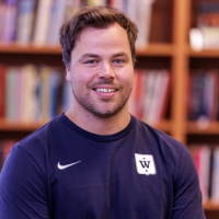 Mann med et vennlig smil ved navn Yngve Apneseth iført en blå sportsskjorte med logo plassert i et bibliotek.