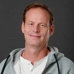En selvsikker, smilende Geir Ove Ovesen i uformelt antrekk mot grå bakgrunn.