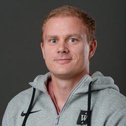 Et portrett av Bjørnar Dolva Bergersen med lyst hår og lys hud, iført en grå hettegenser med synlig logo, og et subtilt smil.