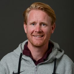En smilende mann med ingefært hår, skjegg, og iført en grå hettegenser med burgunderkrage er Petter Vestheim.