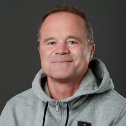 En smilende mann, Erik Jendal, iført en grå hettegenser med et subtilt stjerneemblem mot en grå bakgrunn.