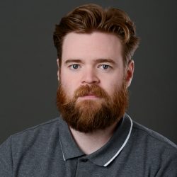 Torleif Kveset, en mann med preparert skjegg og stylet hår, ser rolig på kameraet mot en grå bakgrunn.
