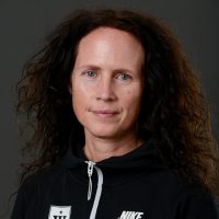 En selvsikker kvinne med langt krøllete hår iført en Marianne Drag-hettegenser, som gir et intenst og fokusert blikk til kameraet.