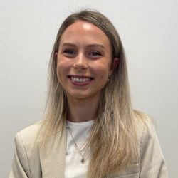En smilende Elise Ø. Torsteinsen, med skulderlangt blondt hår, iført en lys blazer og et halskjede, foran en ensfarget hvit bakgrunn.