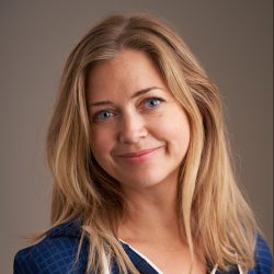 En selvsikker kvinne med et mildt smil, utsmykket med langt blondt hår, stirrer mykt på kameraet mot et nøytralt bakteppe. Dette er Caroline Opdahl Eid.