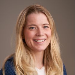 En smilende kvinne med langt blondt hår, iført en blåmønstret topp, satt mot en nøytral bakgrunn.