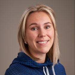 Et portrett av Kaja E.H. Bjørndalen, en smilende kvinne med blondt hår, iført en blå hettegenser, satt mot en nøytral bakgrunn.