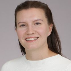 En smilende kvinne med håret trukket tilbake, iført en hvit topp, mot en nøytral bakgrunn.