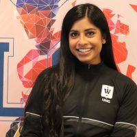 En smilende kvinne i atletisk antrekk poserer foran en fargerik geometrisk bakgrunn med bokstaven "l".