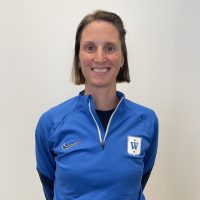 En smilende person iført blå Nike-sportsjakke med Kari Vikhagen Gjeitnes-logo på venstre bryst.