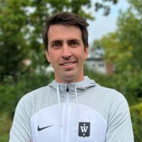 En smilende mann i atletisk klær poserer utendørs.