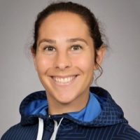 En smilende kvinne kledd i en blå sportsjakke med en hettegenser, ser på kameraet med en vennlig, imøtekommende oppførsel.