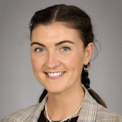 Et profesjonelt hodebilde av en smilende kvinne med mørkt hår, iført en rutete blazer og et perlekjede.