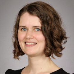 En smilende kvinne med kort brunt hår mot en nøytral bakgrunn.